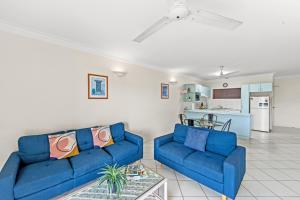 a living room with two blue couches and a kitchen at Koala Court Holiday Apartments in Cairns