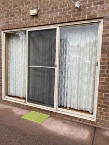 two windows with white curtains on a brick building at Bethel Homestay in Watsonia North
