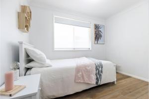 a white bedroom with a bed and a window at Driftwood Cottage 1 28 Farm Rd pet friendly Wi Fi Air Con and ground floor in Fingal Bay
