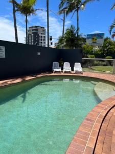 a swimming pool with two lawn chairs and palm trees at Sea Mist Palms in Gold Coast
