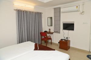 1 dormitorio con 1 cama, TV y silla en Cosy Banjara Guest House, en Hyderabad