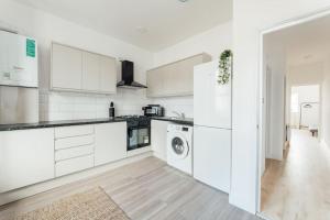 a kitchen with white cabinets and a washer and dryer at Stylish 2 Bedroom Flat in Ilford, London in Ilford