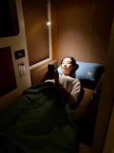 una mujer acostada en la cama mirando su celular en sleep 'n fly Sleep Lounge & Showers, NORTH Node - TRANSIT ONLY, en Doha