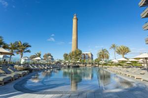 a pool with chairs and a tower in the background at Hotel Faro, a Lopesan Collection Hotel - Adults Only in Maspalomas