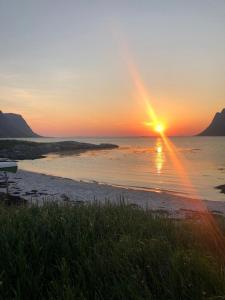 a sunset on a beach with the sun setting over the water at Rystad Lofoten Camping in Rystad