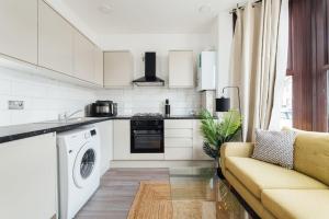 a white kitchen with a couch and a washer at Cosy 2 Bedroom Flat in Ilford, London in Ilford