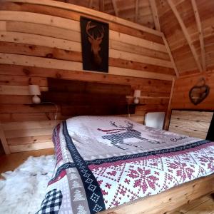 Una cama en una cabaña de madera con un edredón. en Le Kota Montagne en Les Poulières