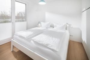 een witte slaapkamer met een groot wit bed met witte lakens bij Seebär Norderney in Norderney