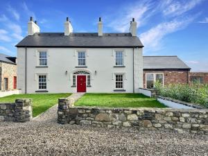 a white house with a red door and a stone wall at The Farmhouse at Corrstown Village in Portrush