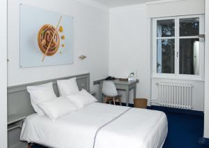 a bedroom with a white bed with a desk and a window at Hotel restaurant au gourmet in Drusenheim