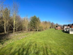 a large green field with trees and a house at Chestnut Lodge With Hot Tub in Malton