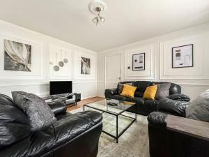 a living room with black leather couches and a television at Newly Refurbished 3 Bed House Near London o2 Arena in London