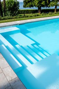 a blue swimming pool with a shadow on the ground at Appartamenti Villa Andrea in Garda