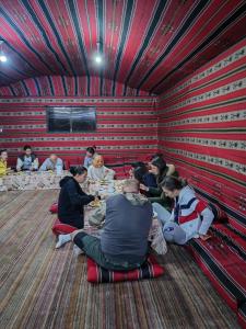 un grupo de personas sentadas alrededor de las mesas en una habitación en Namla Bedouin Camp en Umm Şawwānah