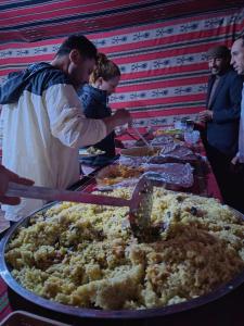 un grupo de personas de pie alrededor de un buffet de comida en Namla Bedouin Camp en Umm Şawwānah