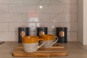 two coffee mugs sitting on a wooden cutting board at Charles Alexander Short Stay - Botanical House in Cleveleys