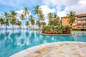 une piscine bordée de palmiers et un bâtiment dans l'établissement Sauipe Grand Premium Brisa - All Inclusive, à Costa do Sauipe