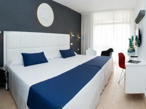 1 dormitorio con 1 cama blanca grande con almohadas azules en Evenia Olympic Garden, en Lloret de Mar