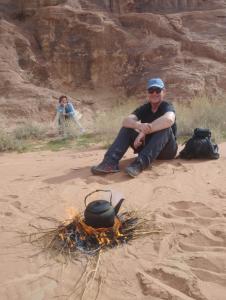 a man sitting on the ground next to a camp fire at Al Raha Luxury Camp in Wadi Rum