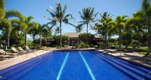 a swimming pool with palm trees and a house at Mauna Lani Kamilo Home 424 in Waikoloa