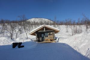 mały domek w śniegu na śnieżnym polu w obiekcie Naali Mökki w mieście Kilpisjärvi