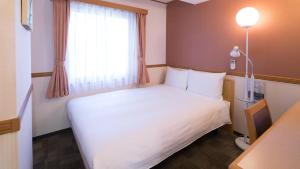 um quarto de hotel com uma cama branca e uma janela em Toyoko Inn Kumamoto-jyo Toricho Suji em Kumamoto