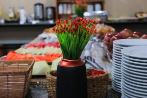a vase filled with red flowers on a table with plates at Hotel Pousada da Lapa in Bom Jesus da Lapa