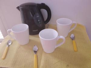 four white cups and spoons on a table with a tea pot at Alquiler temporario Catamarca in San Fernando del Valle de Catamarca