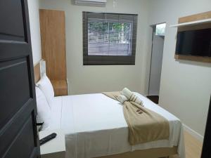 1 dormitorio con cama blanca y ventana en Pousada Emilly en Joinville