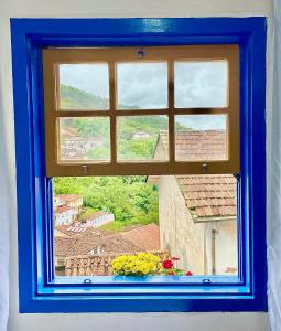 a window with a blue frame and a vase of flowers at Casa charmosa no Centro Histórico com garagem in Ouro Preto