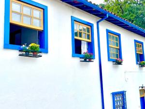 a white house with blue windows and potted plants at Casa charmosa no Centro Histórico com garagem in Ouro Preto