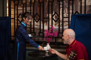 Una mujer le está dando a un hombre una taza de café. en Madelise Palace Hotel & Spa, en Hanói