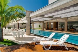 a group of white chairs and a swimming pool at Apartamento Le Jardin - Suítes para Temporada in Caldas Novas