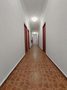 un couloir vide avec des murs blancs et des portes rouges dans l'établissement Warisan Family inn @ Seafront, à Semporna