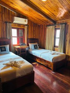 a bedroom with two beds and a table and two windows at Khounphet Heritage House in Luang Prabang
