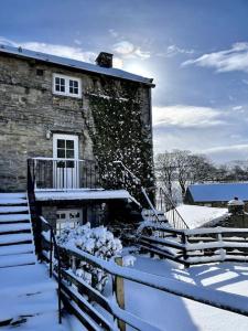 een stenen gebouw met sneeuw op de grond naast een hek bij The Granary, Old Corn Mill, Yorkshire Dales in West Burton