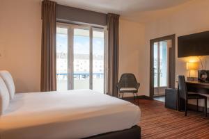 a hotel room with a bed and a desk and a window at The Originals City, Hôtel de l'Europe, Saint-Nazaire in Saint-Nazaire