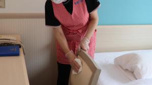 a woman wearing a red and white apron standing next to a bed at Toyoko Inn Futamatagawa-eki Kita-guchi in Yokohama