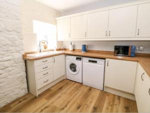 eine Küche mit weißen Schränken und einer Waschmaschine in der Unterkunft Babbling Brook Cottage in Stony Middleton + 12 Fotos