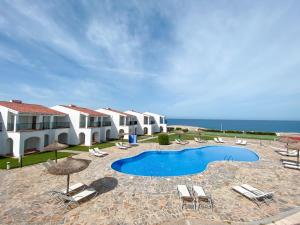 a resort with a swimming pool and chairs and the ocean at RVHotels Sea Club Menorca in Cala en Blanes