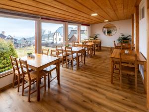 um restaurante com mesas e cadeiras de madeira e janelas grandes em Chata u kostela em Kořenov