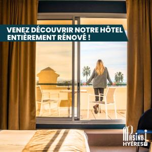 a woman standing on a balcony looking out of a window at Casino Hôtel des Palmiers in Hyères