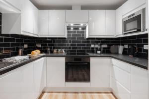 una cocina blanca con paredes de azulejos negros y armarios blancos en Victoria Home - 2 Bedroom Wi-Fi Parking Workers, en Hyde