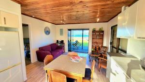 a kitchen and living room with a table and a purple couch at The Sunrise Bach - One Tree Point Holiday Home in One Tree Point