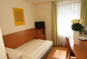 um quarto com uma cama, uma secretária e uma televisão em Memphis Hotel em Frankfurt