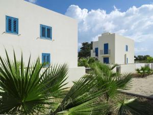 a white building with blue windows and palm trees at Lisca Bianca in San Vito lo Capo