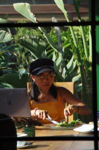 a woman sitting at a table eating food with a laptop at Surfescape Fuerteventura in Lajares