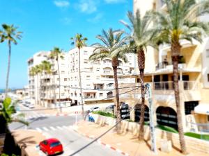 a red car parked in front of a building with palm trees at "In the heart of Acre" from Shneider Apartments in Acre