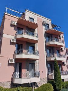 ein rosafarbenes Apartmenthaus mit Balkonen und Büschen in der Unterkunft Apartmani IVANA in Vrnjačka Banja