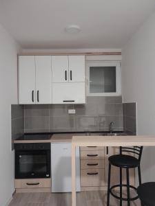 uma cozinha com armários brancos e um balcão com bancos em Apartman Milena Temerin em Temerin